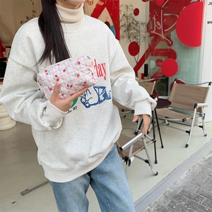 Close-up of quilted cosmetic bag with red cherry pattern held by a model in a cafe