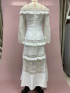 Dettaglio dell'abito lungo in pizzo bianco con spalle scoperte e gonna a balze