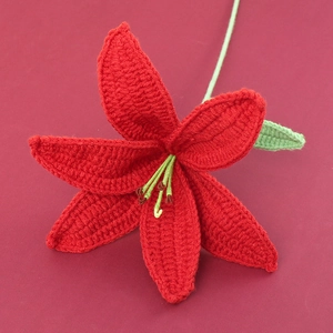 Macro shot of handcrafted red crochet lily with green leaves on a dark red background