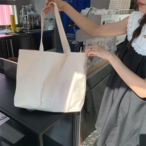 Detail of minimalist cream canvas tote bag held by model, showing texture and large capacity