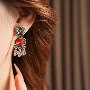 Close-up of vintage silver sunflower earrings with a red gemstone and tassel bells