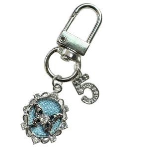 Silver metal keychain with blue butterfly relief, rhinestone circle, and number five pendant