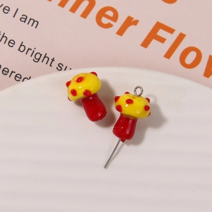 Detailed view of red and yellow glass mushroom earrings on a white textured ceramic tray