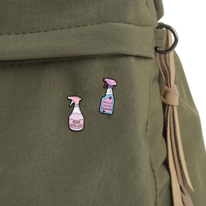 Detail showing two spray bottle enamel pins with funny quotes on green canvas fabric