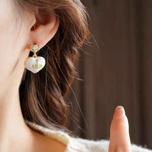 Detail of heart-shaped gold earring with white enamel and crystal on a model ear