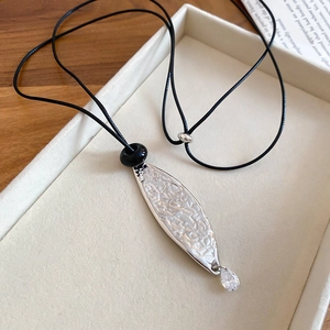 Detail of silver textured pendant with water drop crystal on black leather cord