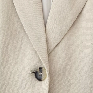 Macro shot of beige linen vest with tortoise pattern buttons and textured weave fabric