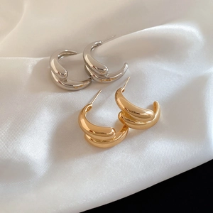 Detail of C-shaped drop earrings in gold and silver finish on white silk background