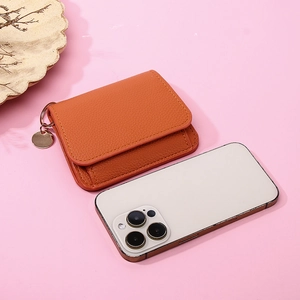 Top view of orange pebbled leather wallet with circular metal pendant on pink surface