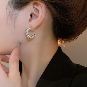 Detailed view of silver C-shaped earrings with pearls and crystals on a model's ear