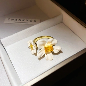 Detailed macro view of golden flower ring with white enamel petals and yellow zircon