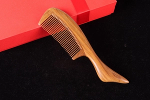 Close-up of a natural green sandalwood comb with fine teeth and a curved handle on velvet