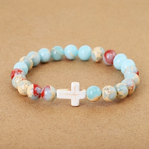 Blue and beige beaded stone bracelet with white cross charm on a brown textured surface