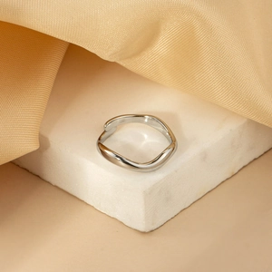 Polished silver wave ring on marble display with silk fabric, minimalist jewelry detail