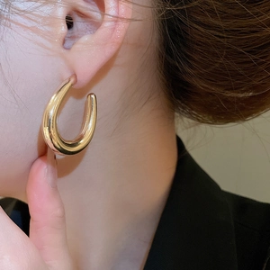 Close-up of minimalist chunky golden U-shaped earring worn on ear with polished finish