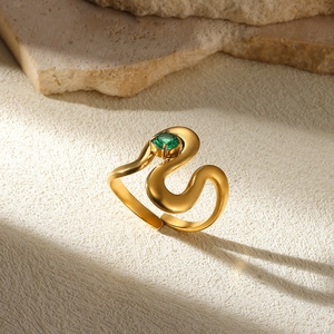 Detail of a wavy gold sculptural ring featuring a round green gemstone on a stone base