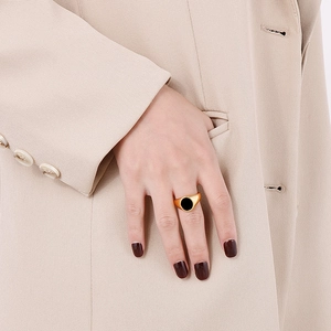 Close-up of a gold minimalist signet ring with a round black enamel inlay on a hand