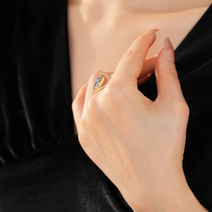 Macro shot of an oval iridescent gemstone set in a wavy gold open ring on finger