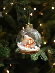 Detalle de bola de Navidad transparente con reno plateado y casita de madera