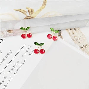 Detail of three cherry enamel brooches with red fruits and heart patterns on white fabric