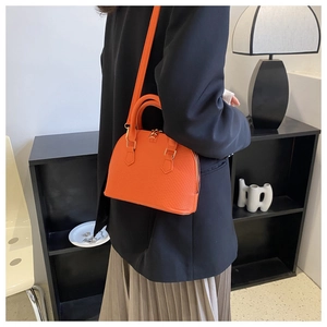 Orange shell-shaped handbag with lychee pattern texture worn by model over black blazer