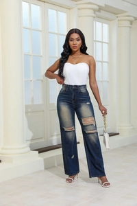 Detail of high-waisted wide-leg jeans with distressed rips and white tube top on model