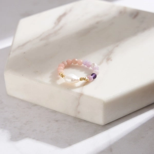 Detailed macro view of baroque pearl and pink purple beaded ring on marble base