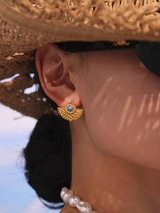 Detailed view of vintage gold fan earrings with blue stone worn by a model