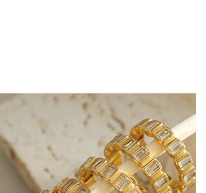 Dettaglio di tre anelli placcati oro 18k con zirconi a taglio baguette su legno