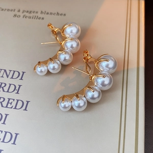 Detailed macro view of curved gold earrings featuring five elegant white pearls