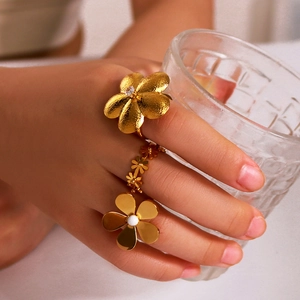 Gold flower rings set with pearls and zircon crystals on a model holding glass