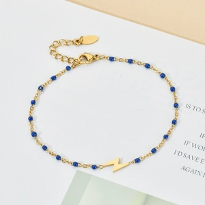 Detail of gold chain bracelet with blue beads and a lightning bolt charm on card