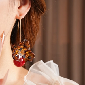 Detail of flower resin earrings with amber petals and red sphere drop on a model