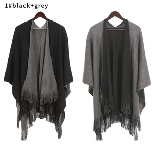 Dettaglio di un poncho reversibile in maglia nero e grigio con eleganti frange sui bordi
