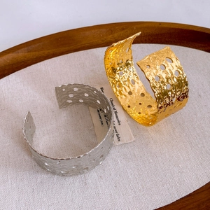 Detalle de brazaletes abiertos chapados en oro y plata con textura martillada y huecos