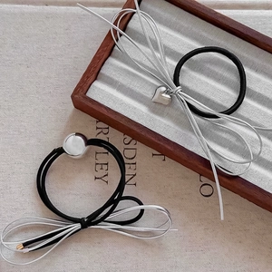 Close-up of black elastic hair ties with silver heart pendants and metallic bows