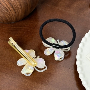 Golden butterfly hair clip and black elastic hair tie set on a wooden surface