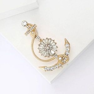 Classic golden nautical anchor brooch with sparkling rhinestones on a white podium