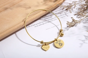 Detail of adjustable gold heart bracelet with Love charm and girl pendant on wooden tray
