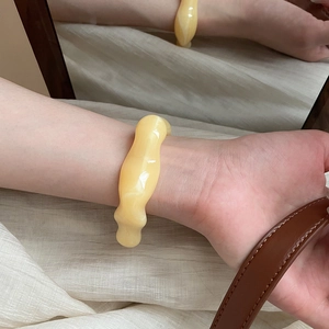 Detailed view of irregular wavy yellow resin cuff bracelet on white textured fabric