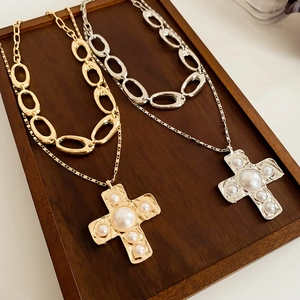 Detailed view of layered cross necklaces in gold and silver with pearls on a wooden tray