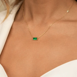 Close-up of gold chain necklace with a rectangular green emerald gemstone pendant