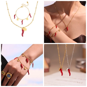 Close-up of red chili and clover charms on gold stainless steel jewelry set