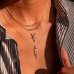 Close-up of layered S925 silver necklaces with colorful crystals on striped shirt