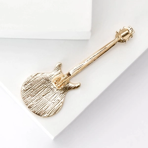 Golden enamel guitar brooch on white geometric prop for fashionable rock style outfit
