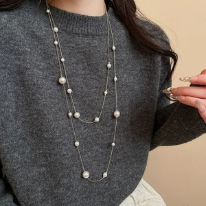 Close-up of double-layer pearl necklace with golden chains on a grey sweater
