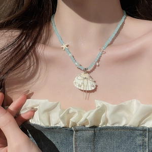 Close-up of ocean-style shell pendant necklace with blue beads and pearls on model