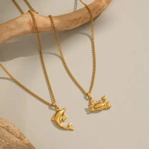 Pendentifs dorés dauphin et crabe sur chaînes gourmettes sur une branche en bois naturel