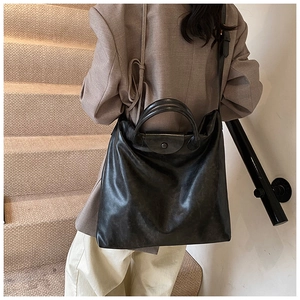 Detail van een grote zwarte leren tote bag over de schouder gedragen op een trap