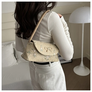 Détail d'un sac d'épaule en paille avec broderie florale et fermoir nœud papillon